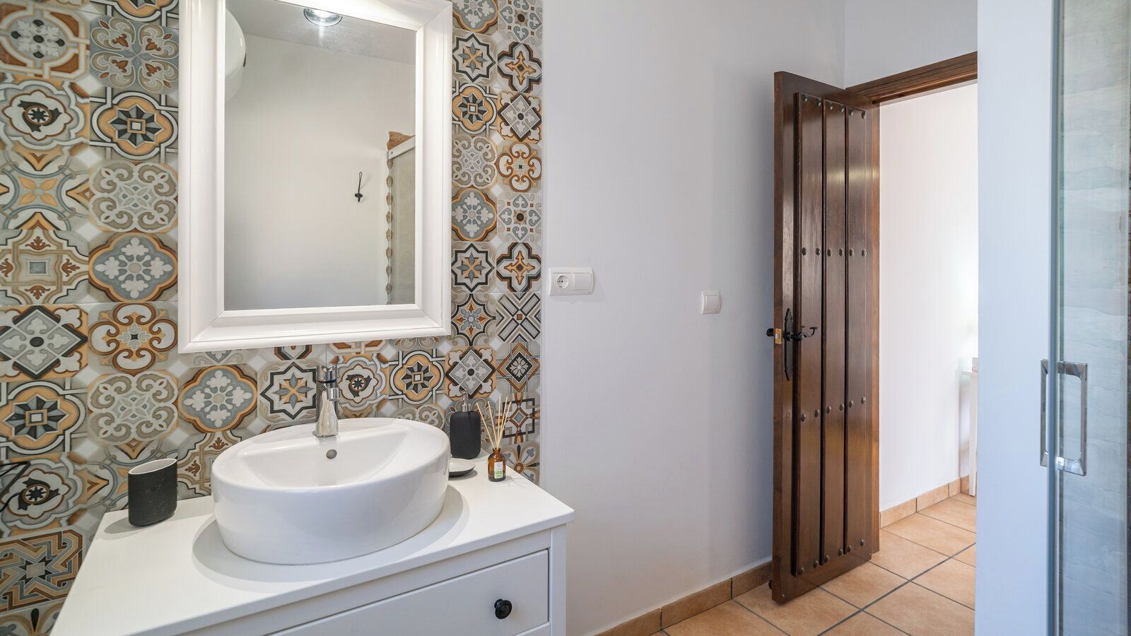 A bathroom with a white sink, a mirror, and patterned tiles on the walls.