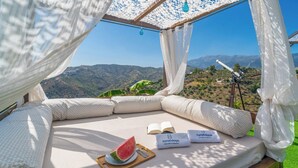 A cozy outdoor seating area with a view of a mountainous landscape, a telescope, and a watermelon on a tray. - El Rincón de Esther Cómpeta by Ruralidays (Málaga)