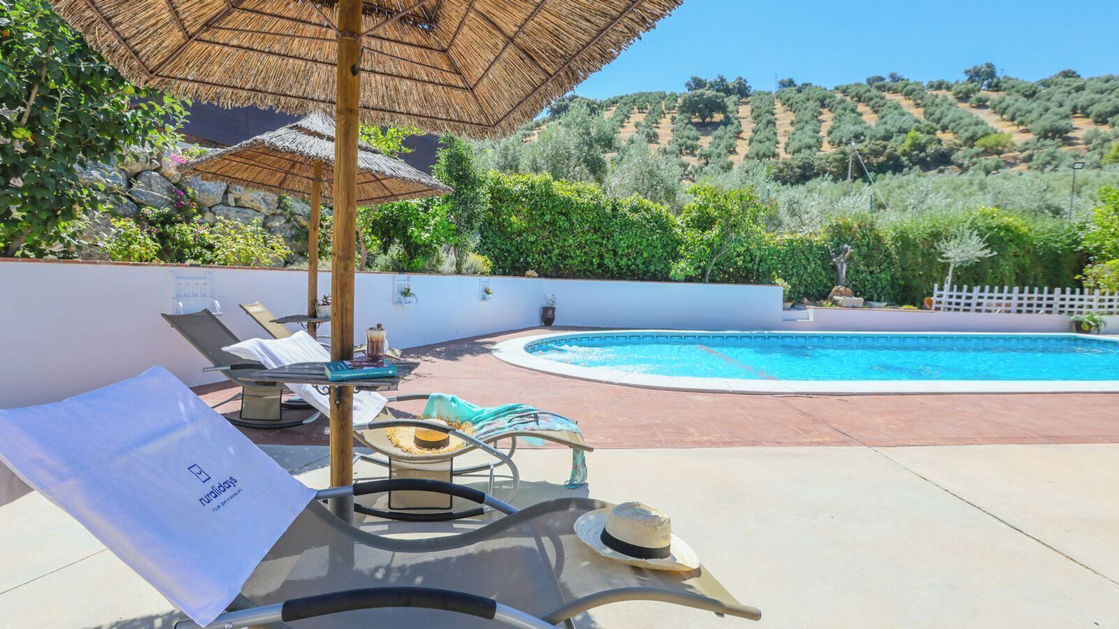 A poolside area with lounge chairs, a table with a drink, and a thatched umbrella.
