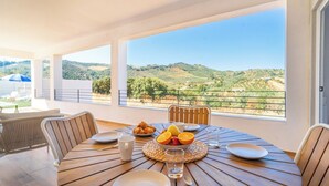 A round wooden table with breakfast items, a view of green hills, and a balcony with chairs. - Puerta del Sol Olvera by Ruralidays (Cádiz)