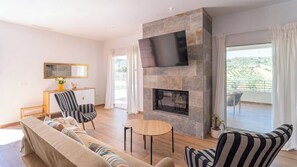 Una sala moderna con un sofá, sillas a rayas, una chimenea, un televisor y un balcón con cortinas.