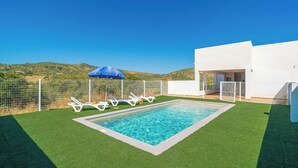 A swimming pool with artificial grass, white lounge chairs, a blue umbrella, and a white building with a door. - Puerta del Sol Olvera by Ruralidays (Cádiz)