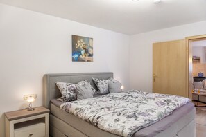 Een slaapkamer met een bed, nachtkastjes, een schilderij en een deur naar een badkamer.