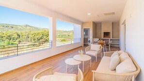 Ein geräumiger Balkon mit Blick auf eine hügelige Landschaft, eine Essecke mit Tisch und Stühlen sowie eine Küchenzeile.