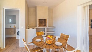 A compact kitchen with a built-in oven, a dining area with a round wooden table, and a washing machine in the adjacent room. - Puerta Encina Olvera by Ruralidays (Cádiz)