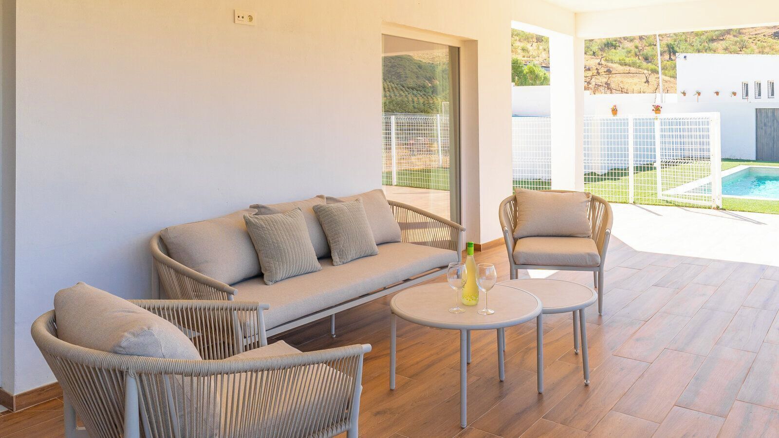 A modern outdoor seating area with a sofa, chairs, and a small table, overlooking a pool and greenery.