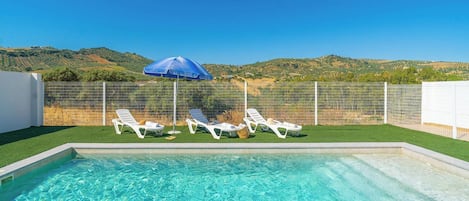 Una piscina con acqua cristallina, circondata da sdraio bianche e un ombrellone blu.