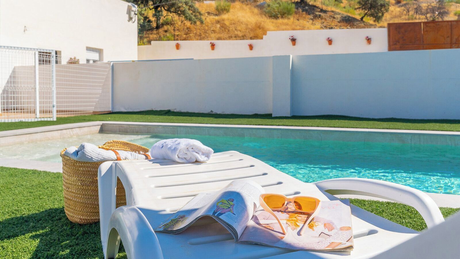 Zona junto a la piscina con una silla de descanso, una toalla y una cesta.