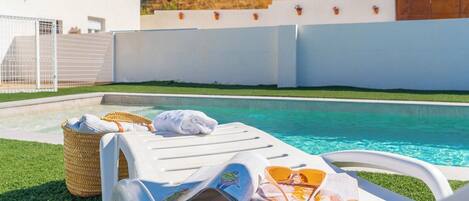 Zona junto a la piscina con una silla de descanso, una toalla y una cesta.