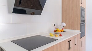 A kitchen with a white countertop, a black induction cooktop, a microwave, and wooden cabinets. - Puerta Encina Olvera by Ruralidays (Cádiz)
