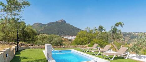 A swimming pool with a view of mountains, surrounded by grass and lounge chairs.
