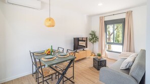 A modern living room with a dining area, a TV, a sofa, and a large window. - Alma de Olivo El Gastor by Ruralidays (Cádiz)