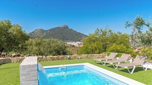 Ein Swimmingpool mit Liegestühlen, einer Steinmauer und Blick auf einen Berg.