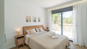 A bedroom with a large bed, a nightstand with a lamp, a window with curtains, and artwork on the wall. - Alma de Olivo El Gastor by Ruralidays (Cádiz)