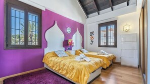 Une chambre avec deux lits, un mur violet et un plancher en bois.