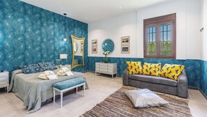 A bedroom with a bed, bench, dresser, and a sofa with patterned cushions. - Casa Rural El Mayorazgo Saleres by Ruralidays (Granada)