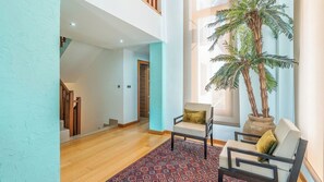 A spacious living area with a wooden staircase, a large potted plant, and a patterned rug.