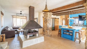 Ein rustikales Interieur mit einer Stein Säule, einem Kamin, einer Couch und einer Küchenzeile.