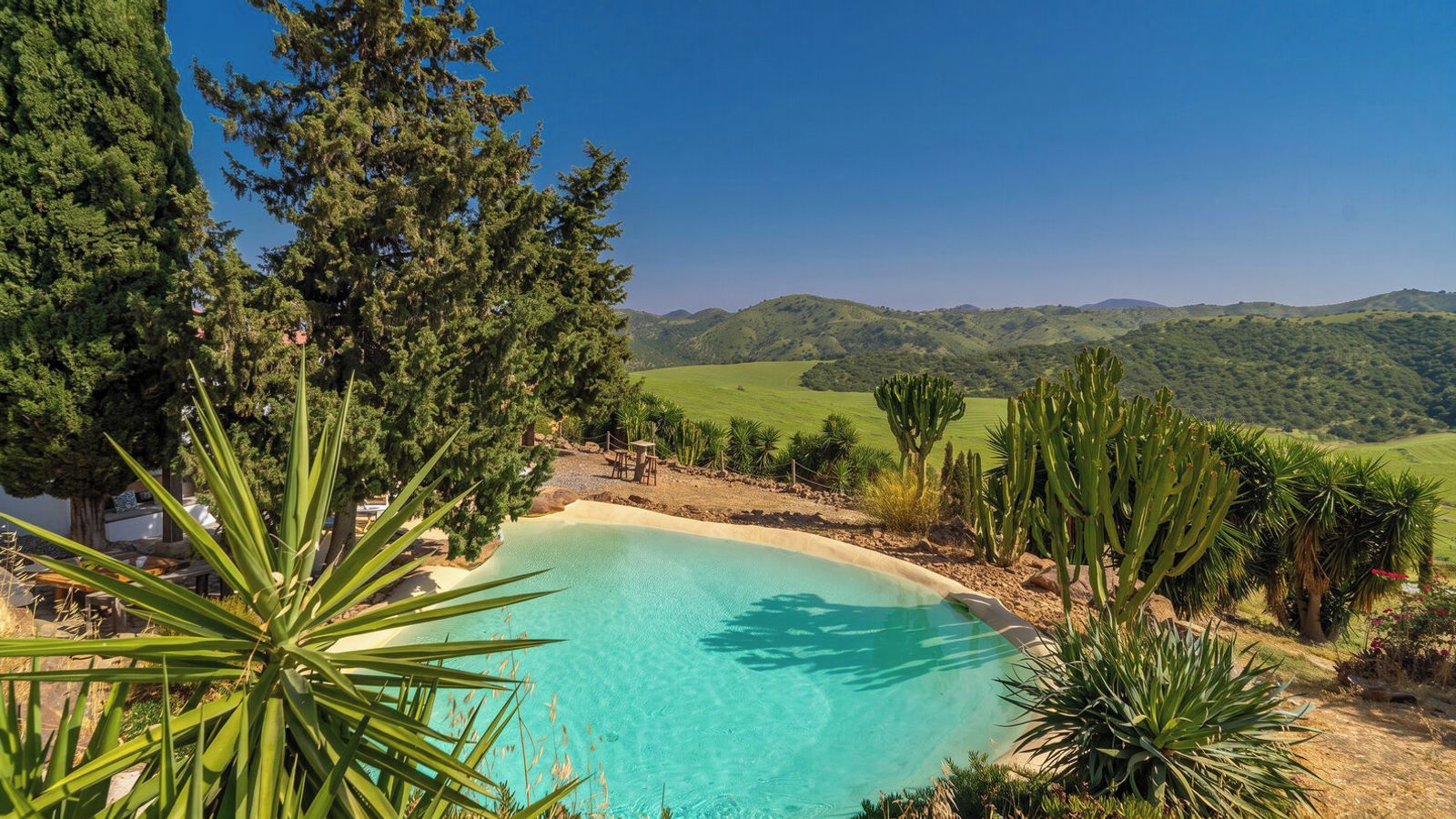 Ein Pool, umgeben von Wüstenpflanzen und Hügeln.