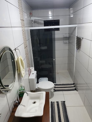 A bathroom with white tiles, a sink, a toilet, a mirror, and a shower area. - Sobrado 02quartos prox Recanto Cataratas (Foz do Iguaçu)