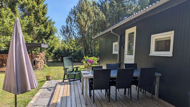 Une terrasse dotée de mobilier d’extérieur, d’une table et de chaises, entourée d’un jardin et d’arbres.
