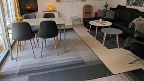 Un salon moderne comprenant un coin repas, un canapé noir, un téléviseur et une fenêtre agrémentée de plantes.