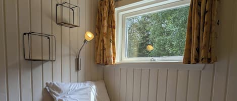 Ein Einzelbett mit weißer Steppdecke, einer Nachttischlampe und einem Fenster mit Vorhängen.