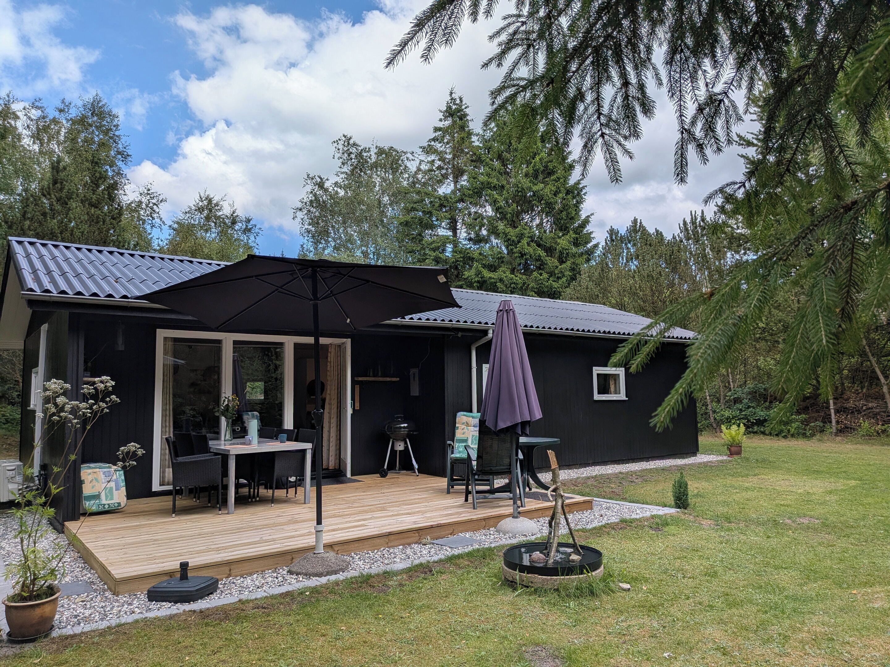 A cabin with a deck, outdoor seating, a grill, and a small garden.