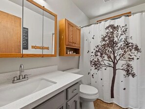 Ein Badezimmer mit Waschbecken, Spiegel, Holzschränken und einem Duschvorhang mit Baummotiv.