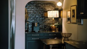 A kitchen with dark cabinetry, a stone archway, a coffee maker, a lamp, and a basket.