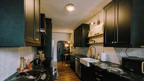 A kitchen with dark cabinets, a wooden floor, a sink, and a countertop with a kettle.