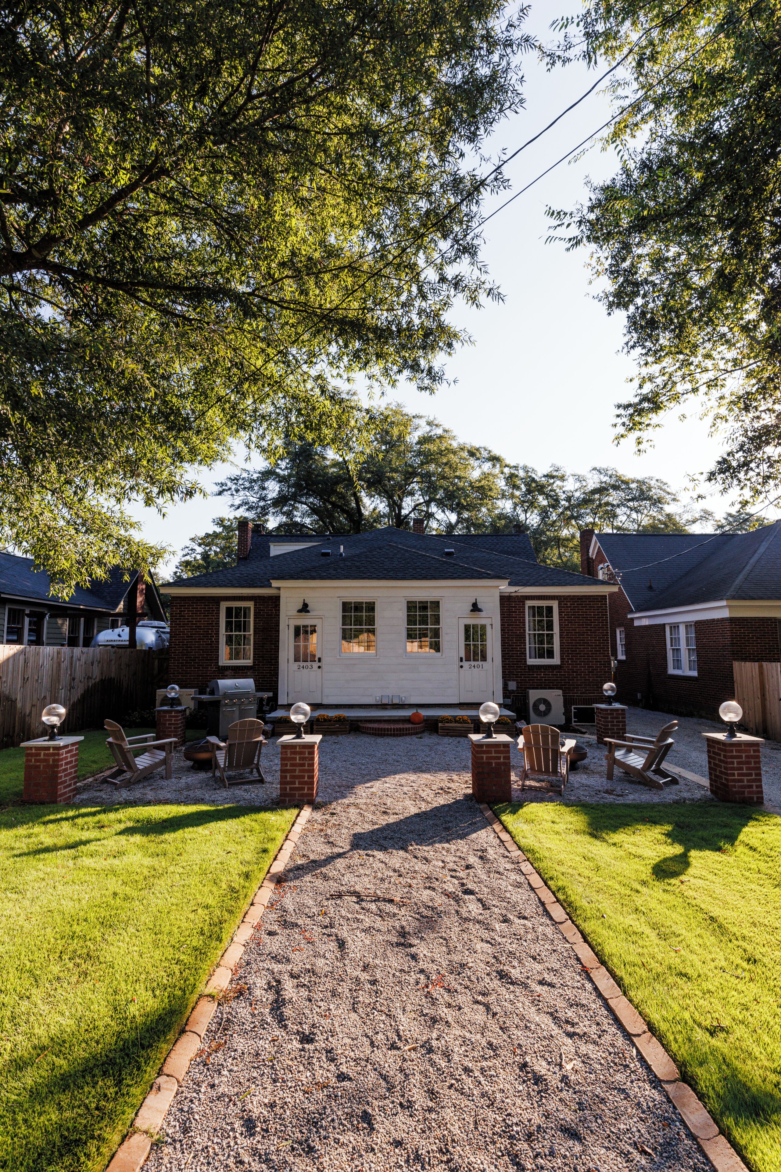 A backyard with a gravel path, brick seating, and a house with a chimney.