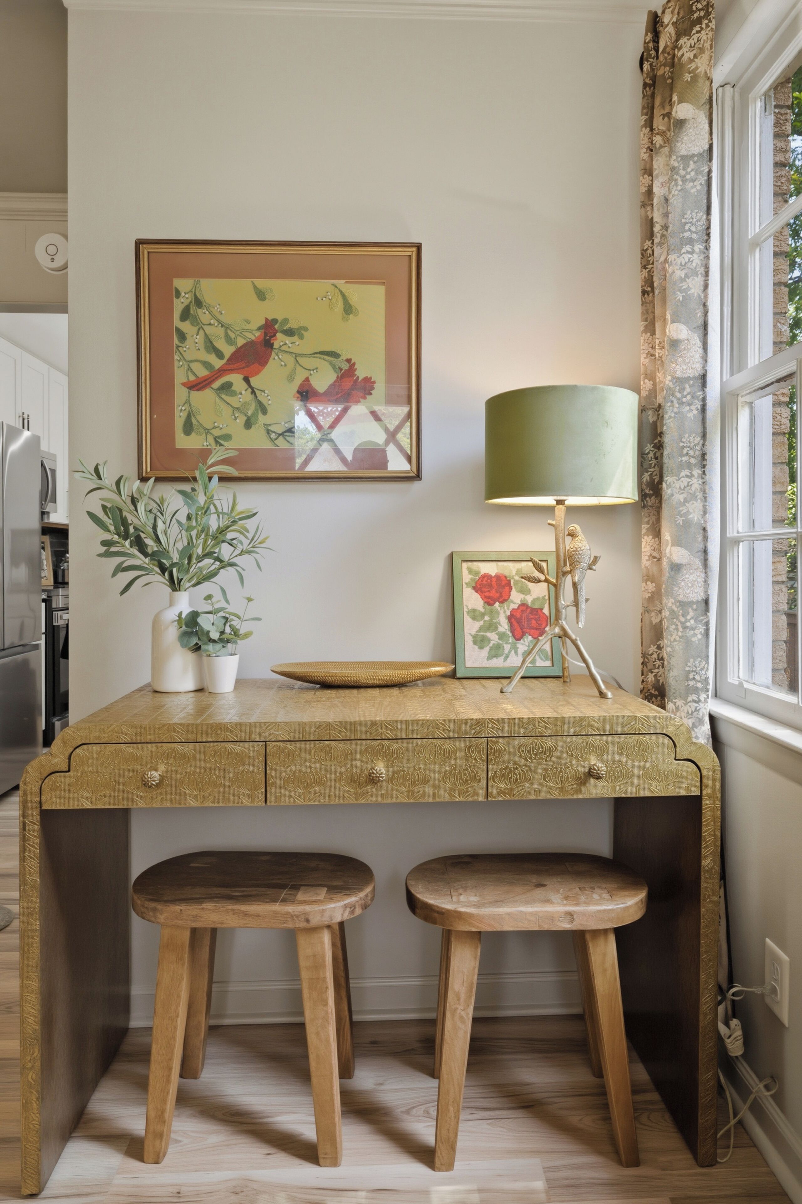 A wooden desk with two stools, a lamp, and framed artwork on the wall.