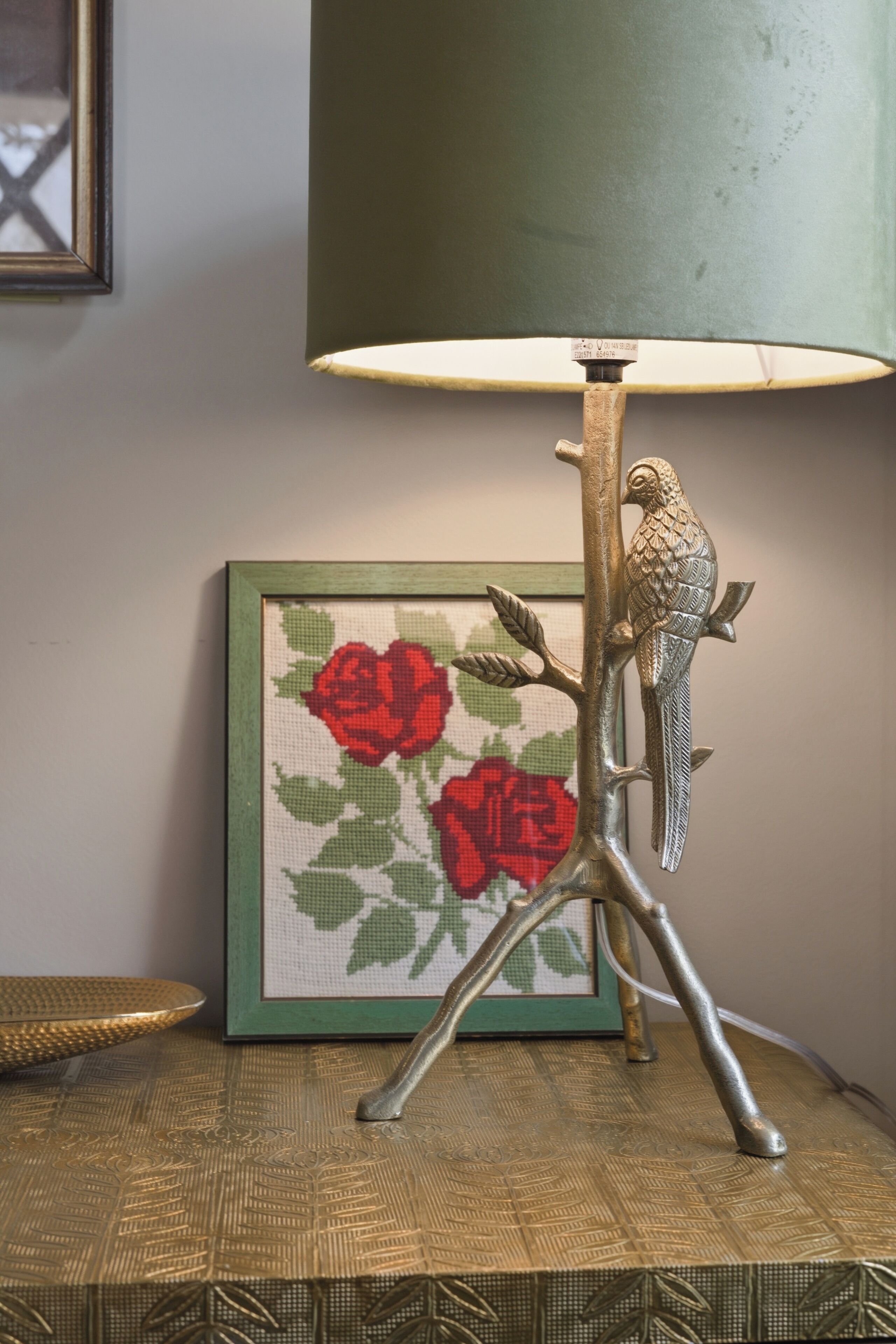 A lamp with a bird design on its stand, a framed picture of red roses, and a textured table surface.