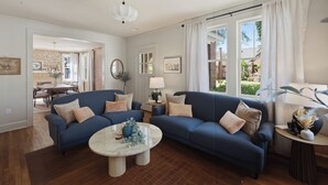A living room with a blue sofa, a round coffee table, and a dining area in the background.