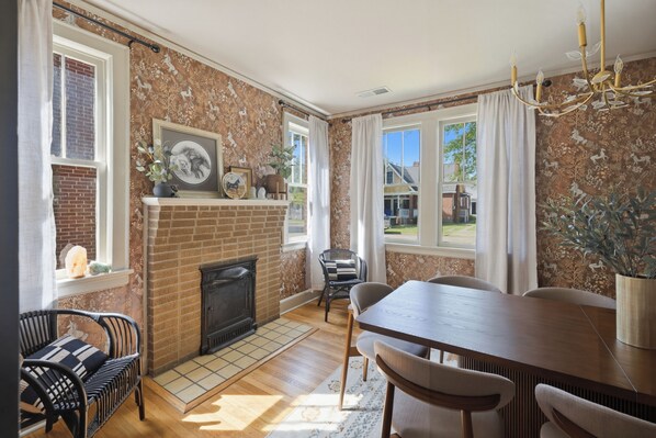 A dining area with a brick fireplace, a chandelier, and a view of the outside.