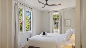 A bedroom with a bed, a ceiling fan, a bedside table with a lamp, and a window with curtains.