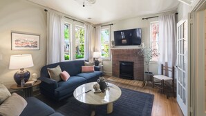 A living room with a sofa, coffee table, fireplace, TV, and large windows.