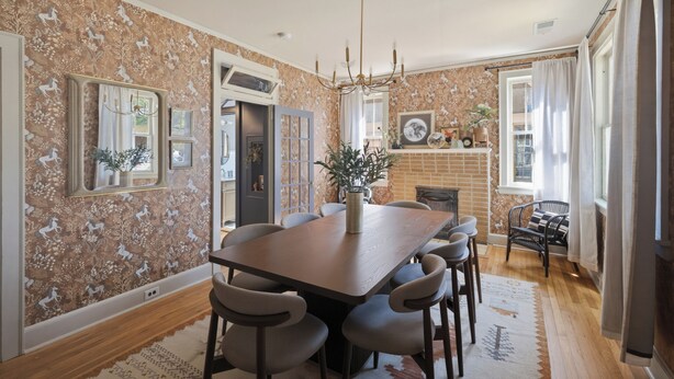 A dining area with a large wooden table, six chairs, a chandelier, and a brick fireplace.