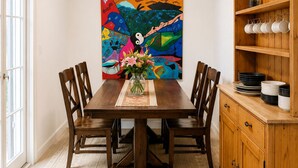 A dining room with a wooden table, chairs, a chandelier, a colorful abstract painting, and a wooden cabinet with dishes. -     Peaceful 1BR Cabin Near Malibu • AC • Pet Friendly (Agoura Hills)