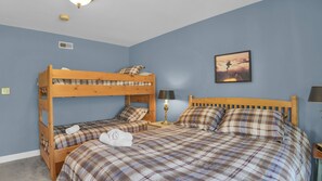 Una stanza con un letto a castello, un letto singolo, una lampada, un quadro appeso e una presa elettrica.
