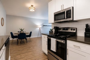 A modern kitchen with a dining area, featuring a stove, microwave, and a dining table with chairs. - Stylish South Tampa Stay | Pool, Gym & King Suites (Tampa)