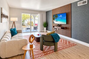 A modern living room with a sofa, armchair, coffee table, and a flat-screen TV mounted on a wall. - Stylish South Tampa Stay | Pool, Gym & King Suites (Tampa)