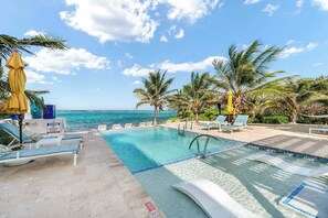 A pool area with clear blue water, lounge chairs, and palm trees. - The Cottages Collection - 10 Oceanfront Suites and 2 BR Penthouse (East End)