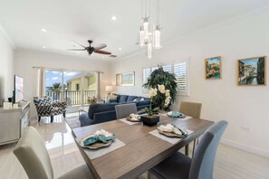 A spacious living area with a dining table set for four, a ceiling fan, and a large window overlooking a balcony. - The Cottages Collection - 10 Oceanfront Suites and 2 BR Penthouse (East End)