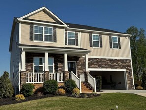 A two-story house with a front porch, a garage, and a stone facade. - Spacious new house in Mebane, NC (Mebane)