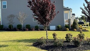 Eenlaags huis met voortuin, gazon en boom met rode bladeren.