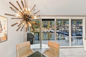 Een moderne eetruimte met een glazen tafel en stoelen, een eigentijdse kroonluchter en uitzicht op een jachthaven door grote schuifdeuren.