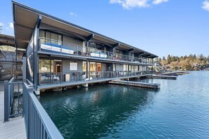 Ein modernes Hotel am Wasser mit mehrstöckiger Bauweise, Balkonen und einem Steg, der ins Wasser führt.