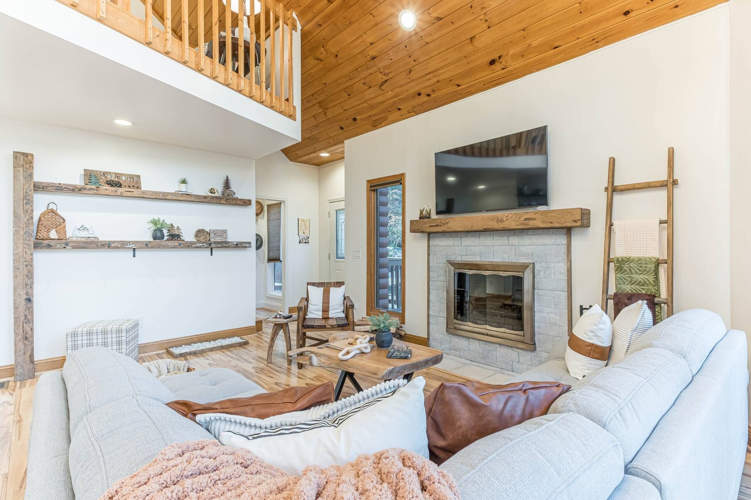 Ein geräumiges Wohnzimmer mit hoher Decke, Holzbalken, Kamin, Fernseher und einer gemütlichen Sitzecke.